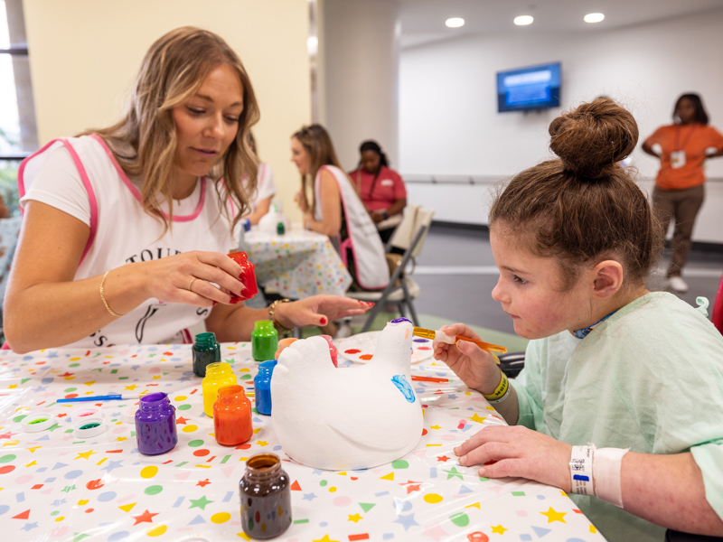 Children's of Mississippi patient Sawyer Coggins of Hamilton paints a chicken tee marker for the Sanderson Farms Championship with Erika Cote, a member of the PGA TOUR Wives Association. Jay Ferchaud/ UMMC Photography